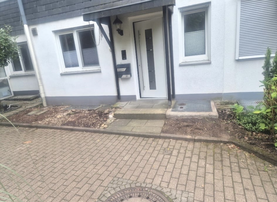 Pflasterarbeiten Langenfeld – Eingang vorher Vorher-Foto Eingang Langenfeld mit Erde neben der Haustür und alter Betonstufe vor den Pflasterarbeiten